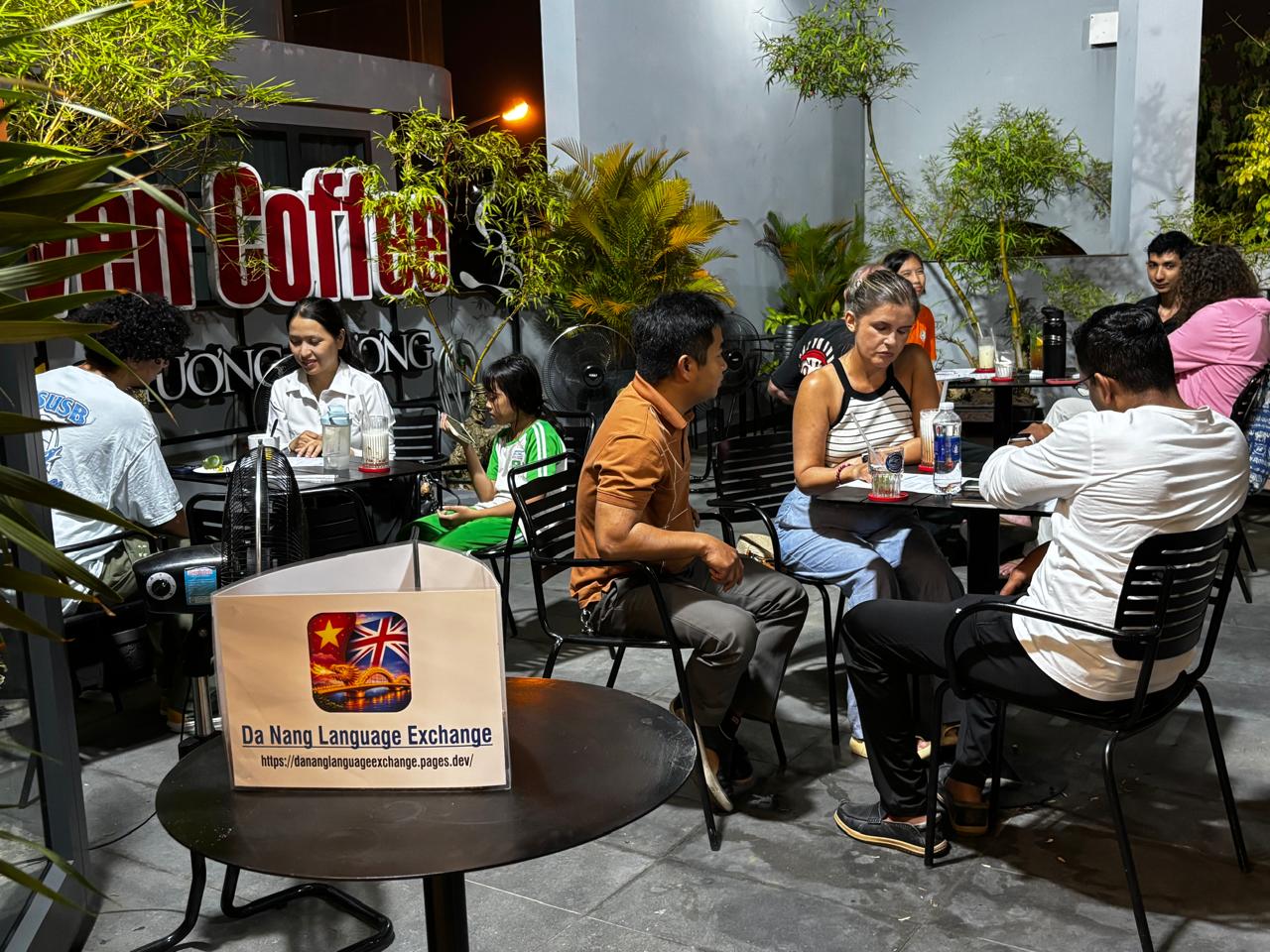 A wide view of multiple small language exchange tables during the Friday, April 17, 2026 session in Da Nang.